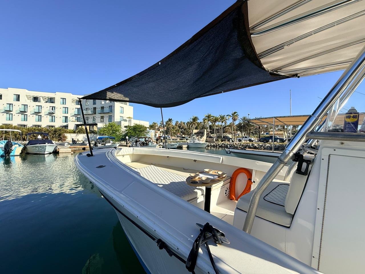 White motorboat docked in harbor with black sun canopy, Mediterranean-style waterfront resort with palm trees in background