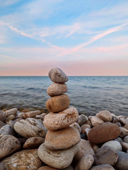 Stack of balanced stones on a pebble beach overlooking calm water at sunset with blue and pink sky