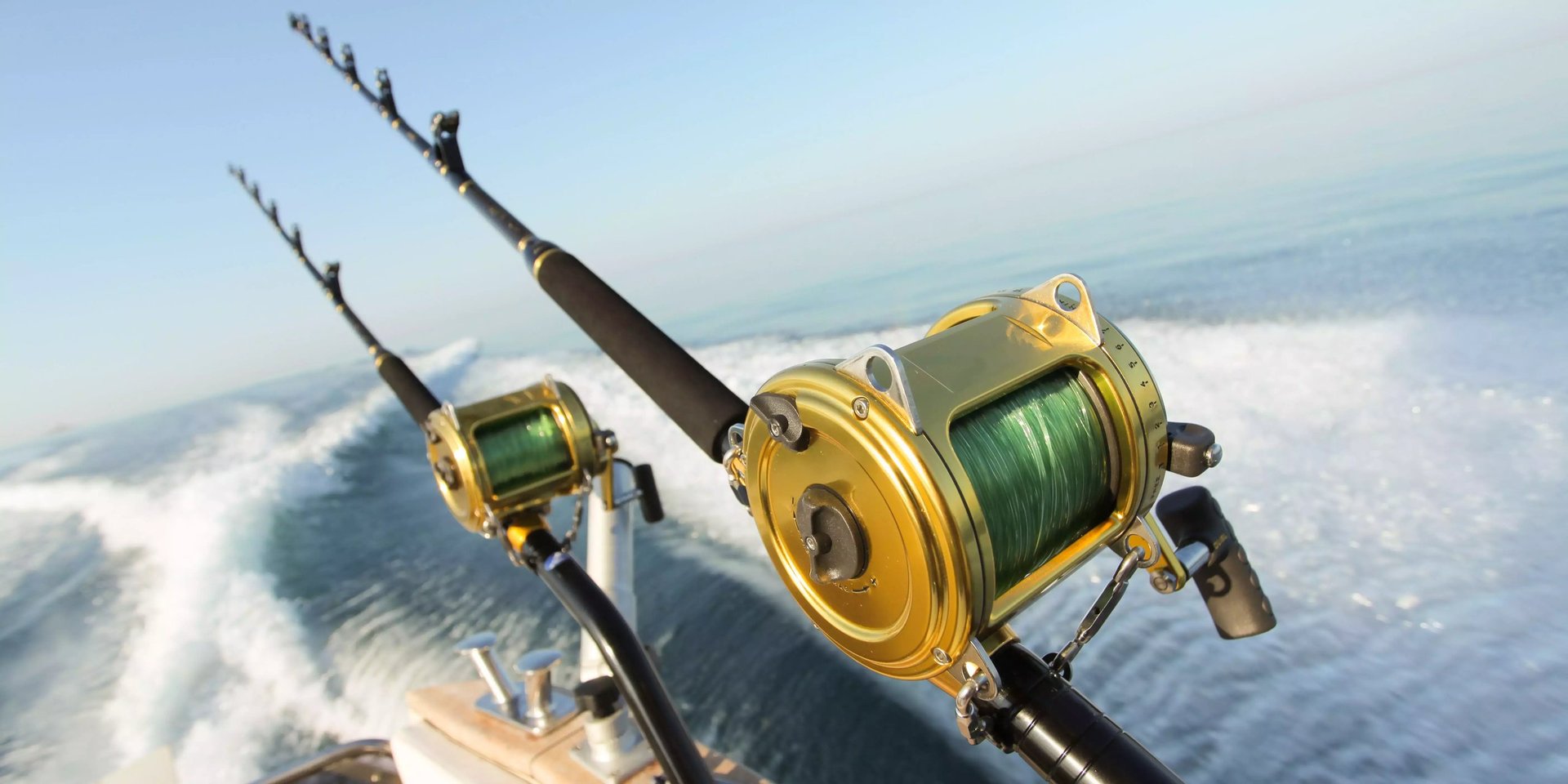 Two gold fishing reels mounted on rods with ocean and cloudy sky in background during deep sea fishing